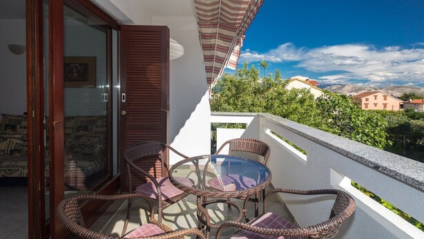 A balcony with wicker furniture and a glass table, overlooking a residential area with houses and trees. - Nice apartment on the first floor with a covered balcony (Baska)