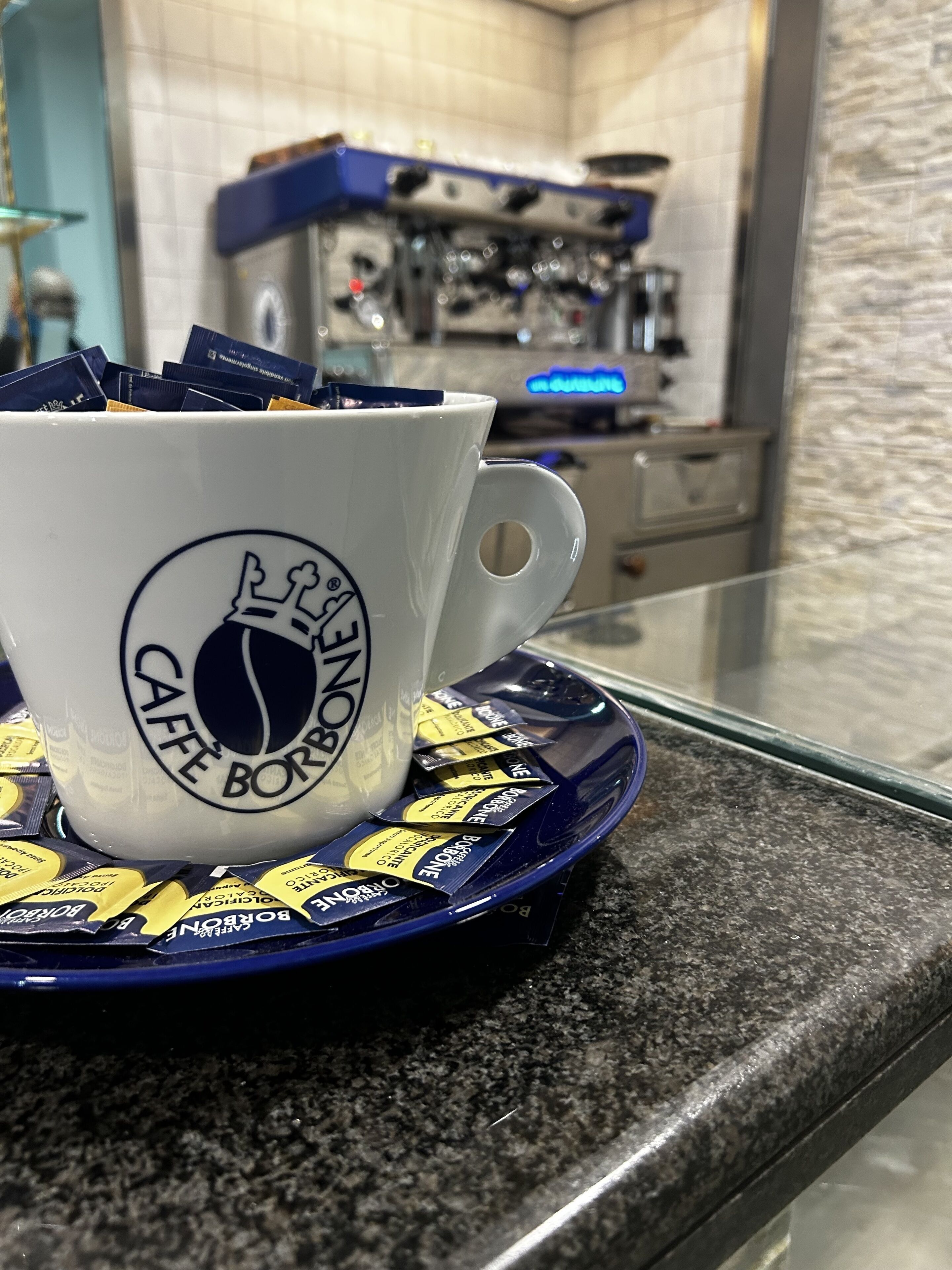 Una tassa de cafè blanca amb un logotip sobre un safata blava, damunt d'un taulell de granit.