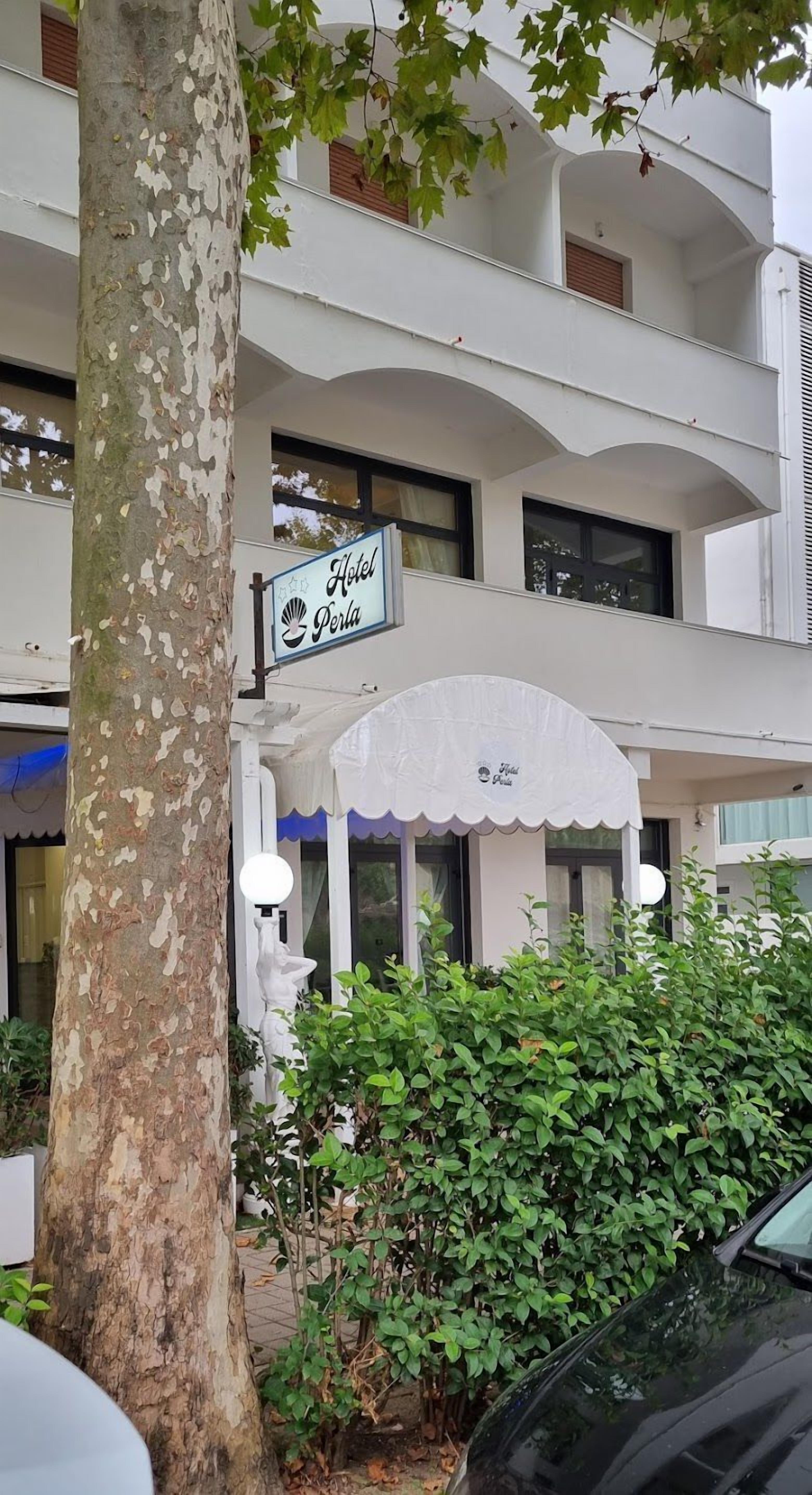 A hotel named "Hotel Perla" with a white facade, a balcony, and a covered entrance.