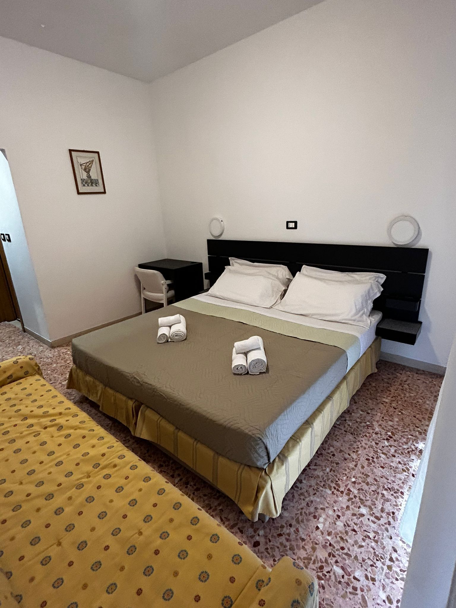 A hotel room with a bed, a bedside table, a chair, and a small desk.