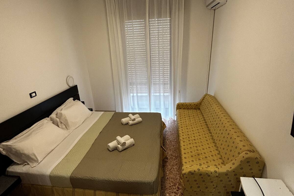 Une pièce comprenant un lit, un petit canapé, un bureau et une fenêtre avec des stores.