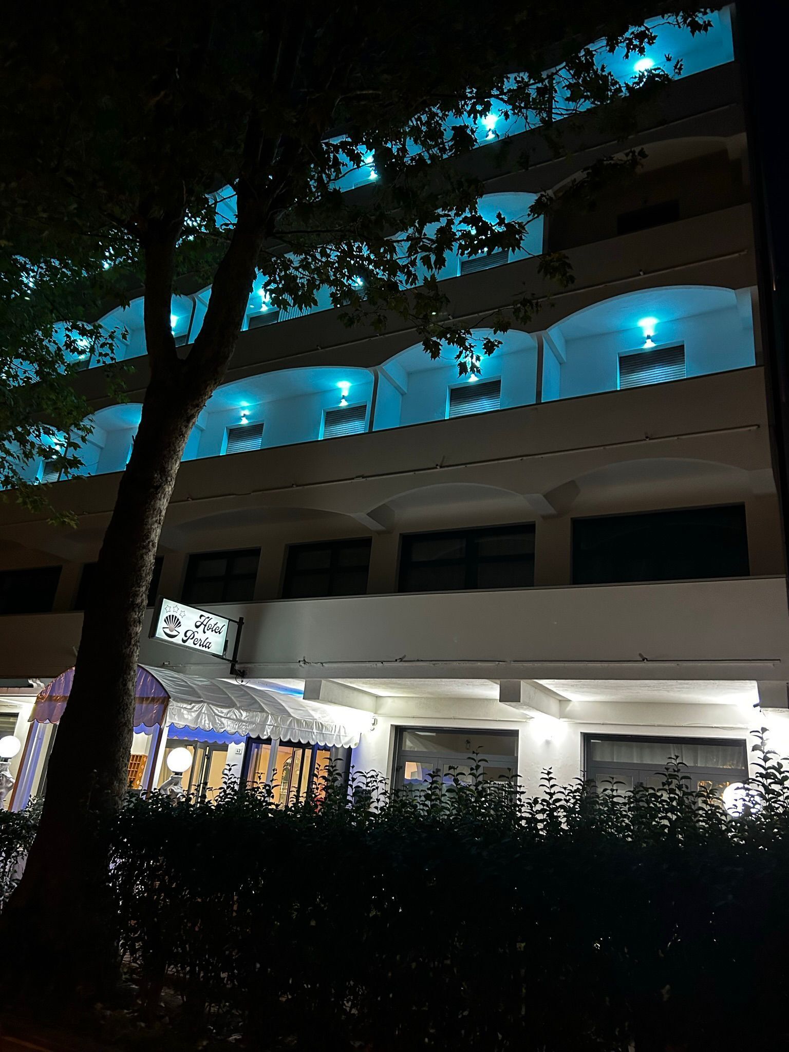Un hotel de varios pisos con balcones, un cartel que indica que es un hotel y una zona cubierta con una carpa.