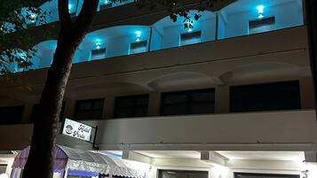Un hotel de varios pisos con balcones, un cartel que indica que es un hotel y una zona cubierta con una carpa.