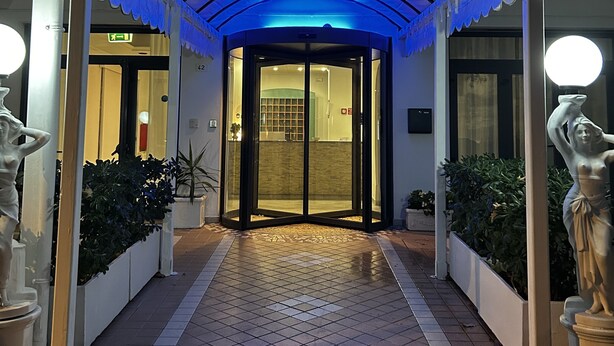 A hotel entrance with a covered walkway, a sign reading "Hotel Perla", and a tiled floor. - Hotel Perla (Cesenatico)