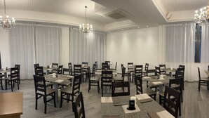 A spacious conference room with multiple tables and chairs, large windows with sheer curtains, and elegant chandeliers. - Hotel Perla (Cesenatico)