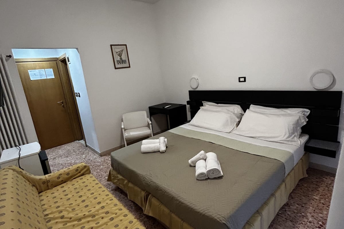 Une chambre d’hôtel avec un lit, une chaise, une table de chevet et une porte.