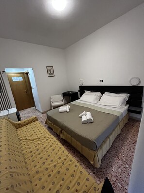 A hotel room with a bed, a chair, a nightstand, and a door. - Hotel Perla (Cesenatico)
