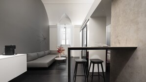 A modern, minimalist interior with a dark wooden floor, a white sofa, a small round table, and two black stools. - Palazzo Giusti Suites and Spa (Urbino)