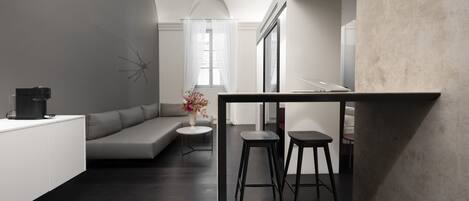 A modern, minimalist interior with a dark wooden floor, a white sofa, a small round table, and two black stools.
