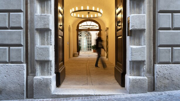 A grand entrance with a large, circular light fixture above a doorway, flanked by stone columns and a tiled floor. - Palazzo Giusti Suites and Spa (Urbino)
