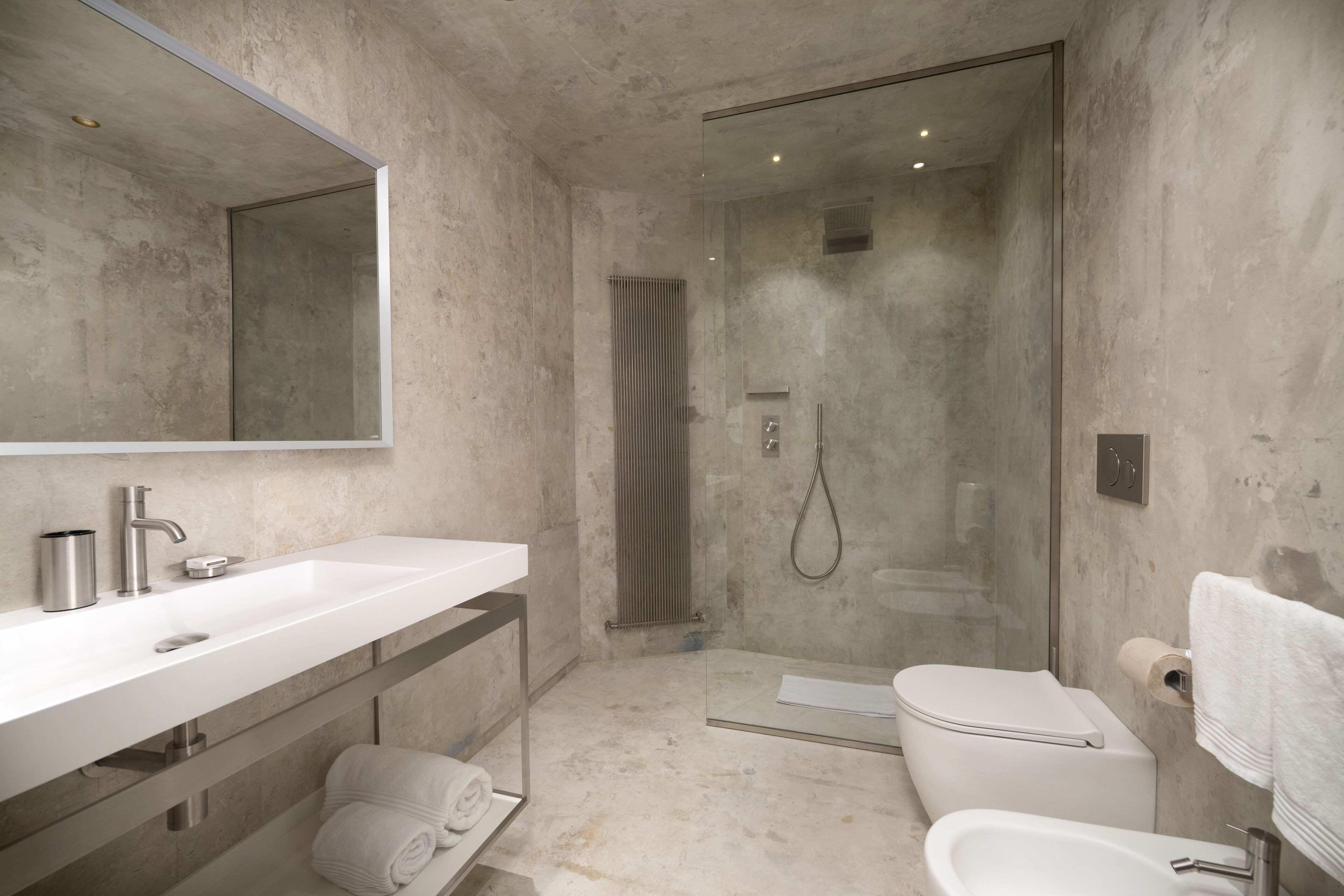 A modern bathroom with a large mirror, a white sink, a glass-enclosed shower, and a white toilet.