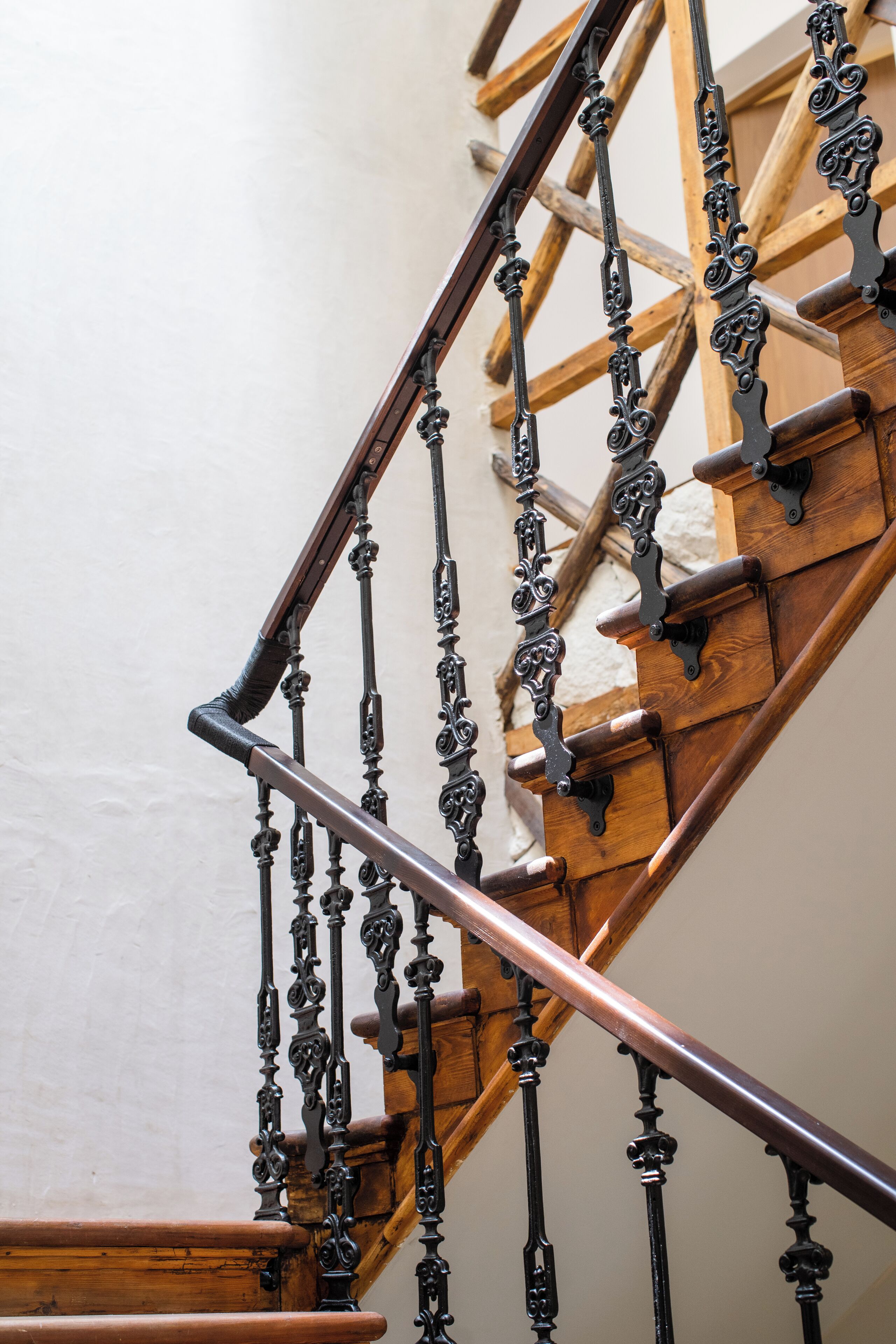 A wooden staircase with ornate black metal railings and a copper handrail.