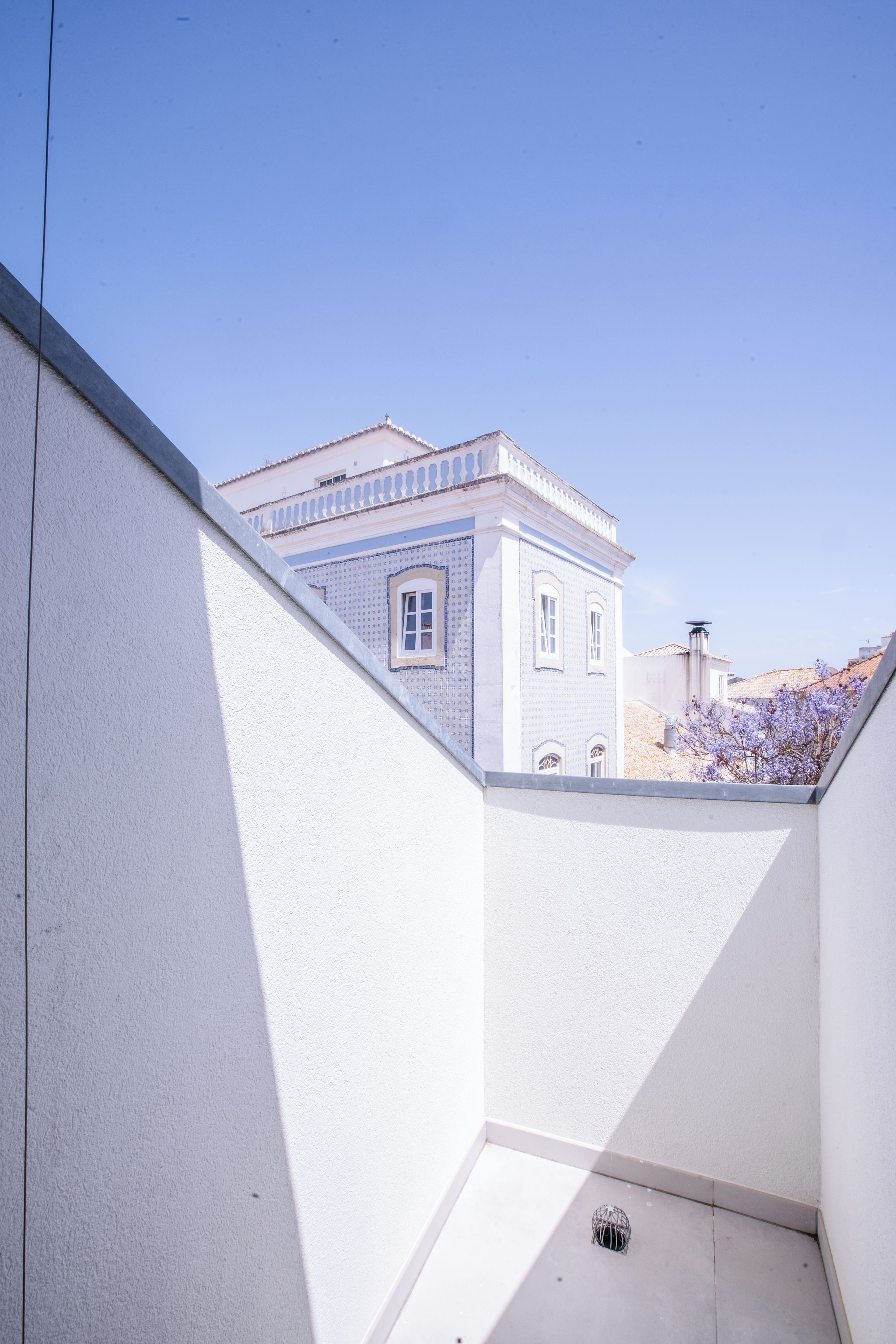 A narrow courtyard with a white wall and a building with blue window frames in the background.