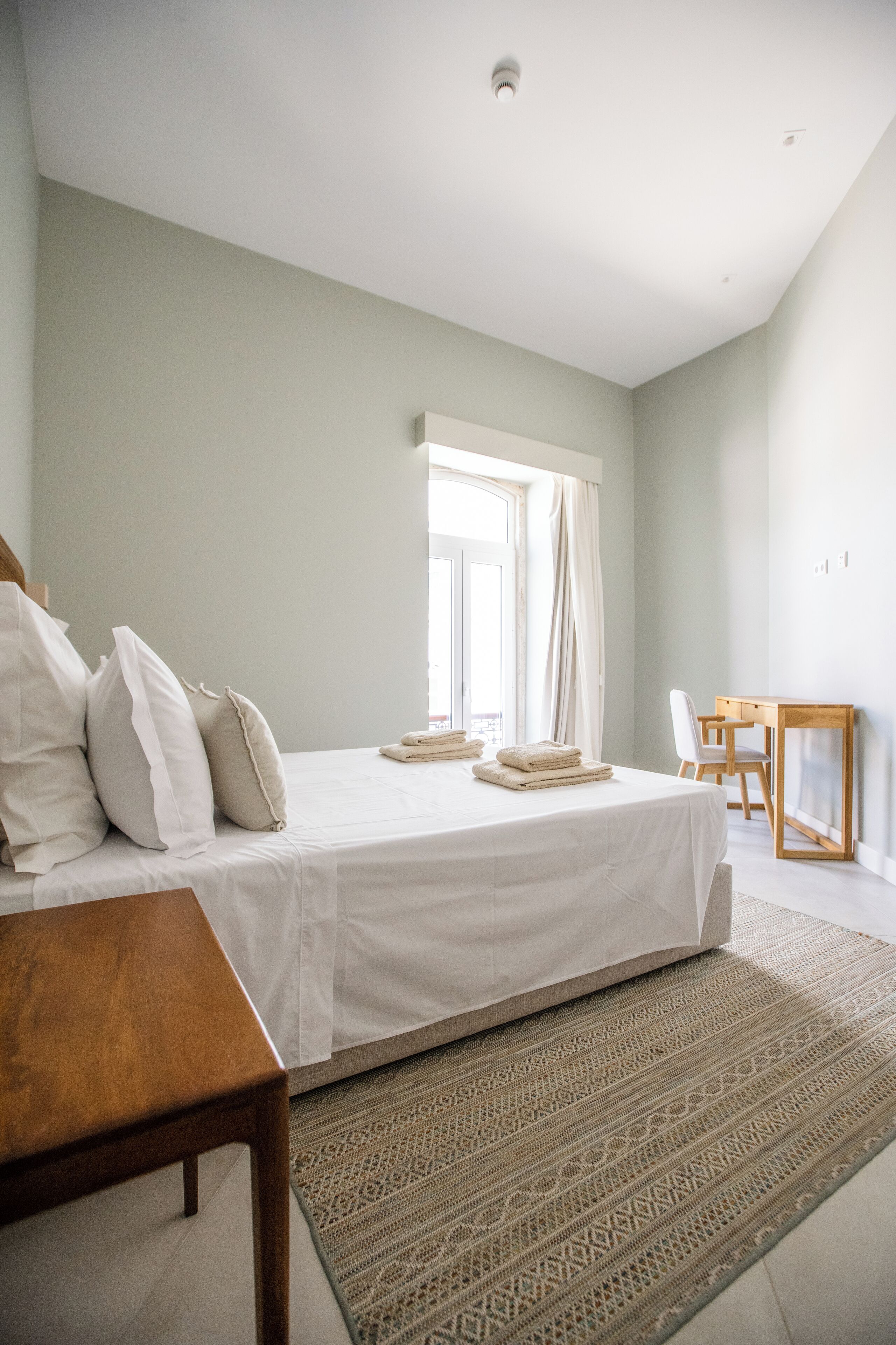 Une chambre à coucher avec un lit, une table en bois, une chaise, un bureau et un tapis à motifs.