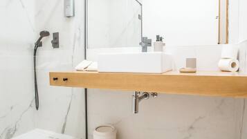 A modern bathroom with a glass shower enclosure, a wooden vanity, a large mirror, and a marble-tiled floor.