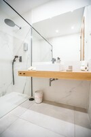 A modern bathroom with a glass shower enclosure, a wooden vanity, a large mirror, and a marble-tiled floor.