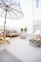A modern outdoor seating area with a white umbrella, a sofa, lounge chairs, and potted plants.
