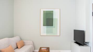 Ein Wohnzimmer mit einer Couch, einem Couchtisch, einem Fernseher und einem gerahmten Kunstwerk an der Wand.