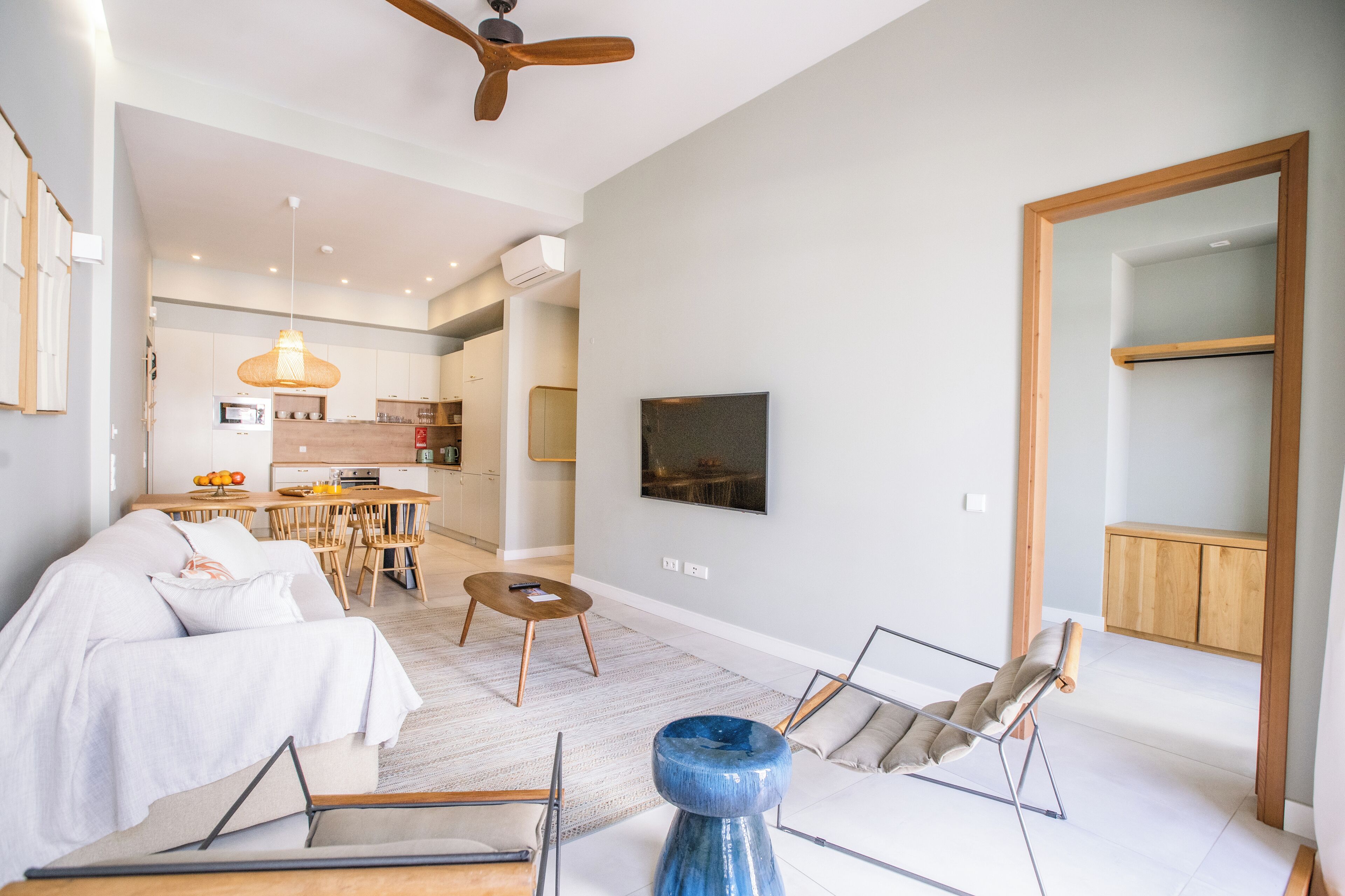 A modern living room with a sofa, coffee table, and a blue accent piece. There is a dining area with a table and chairs, and a kitchen in the background.