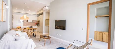 A modern living room with a sofa, coffee table, and a blue accent piece. There is a dining area with a table and chairs, and a kitchen in the background.