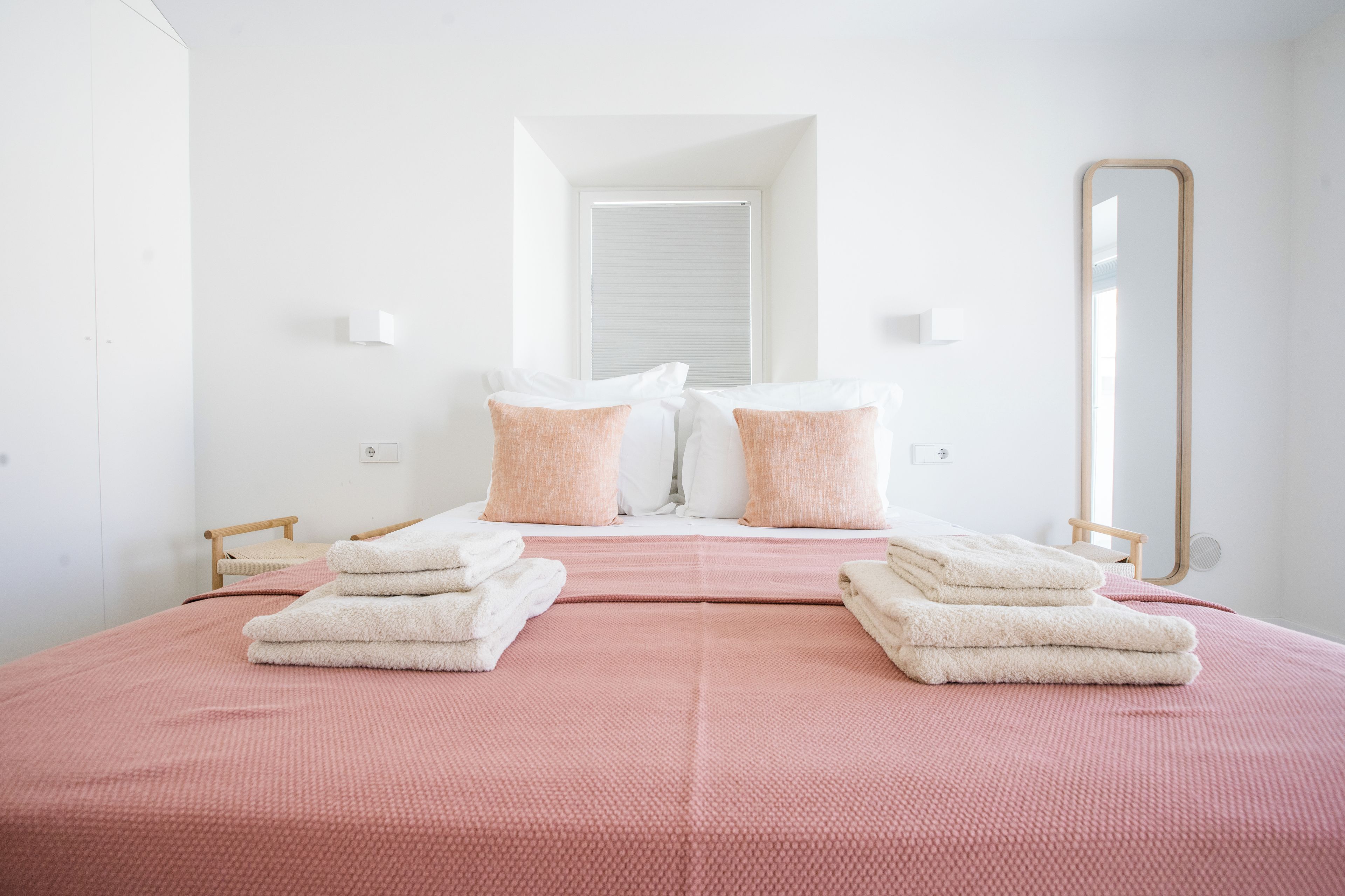 A hotel room with a bed, two pillows, a mirror, and a window.