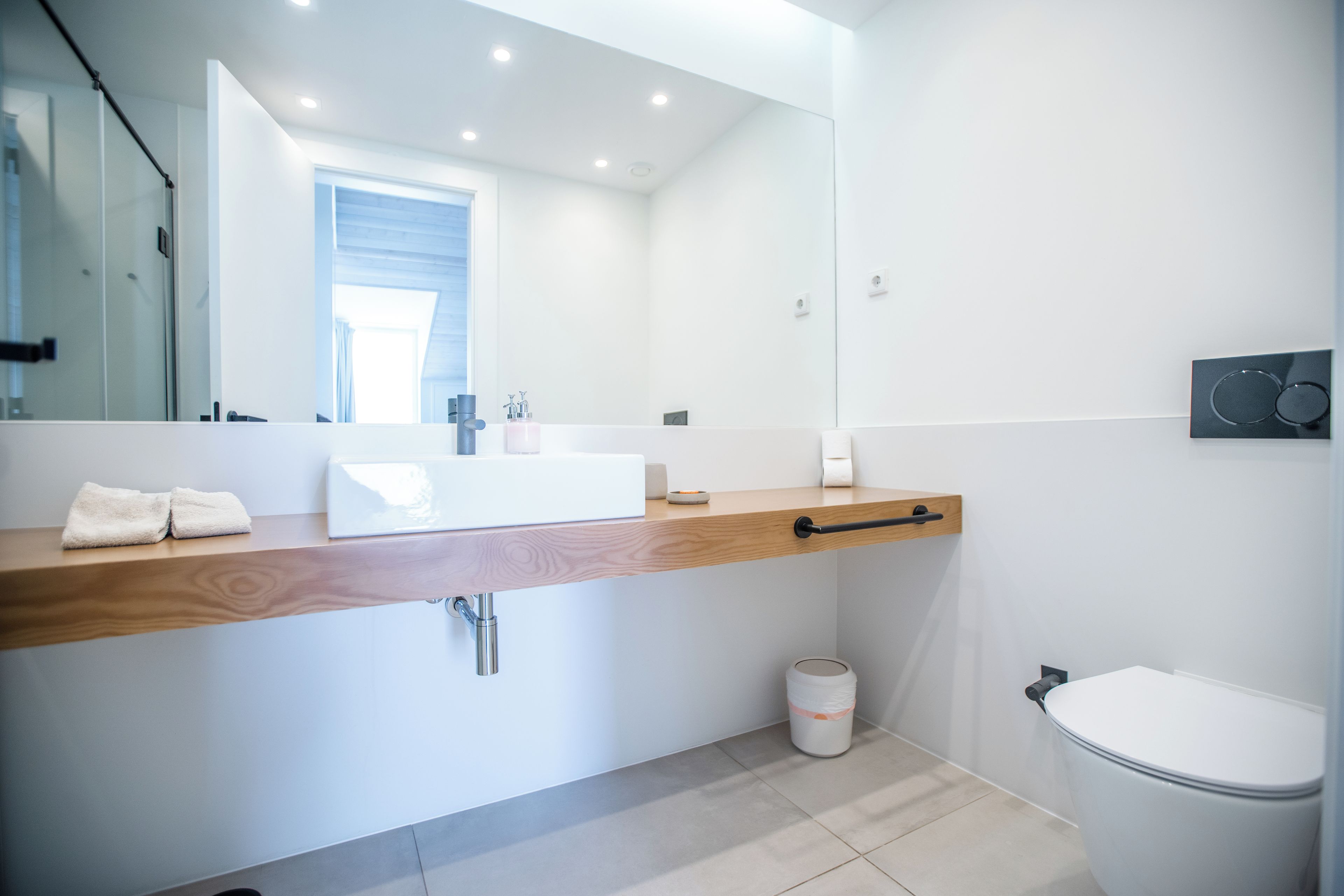 A modern bathroom with a wooden vanity, a white sink, and a large mirror.