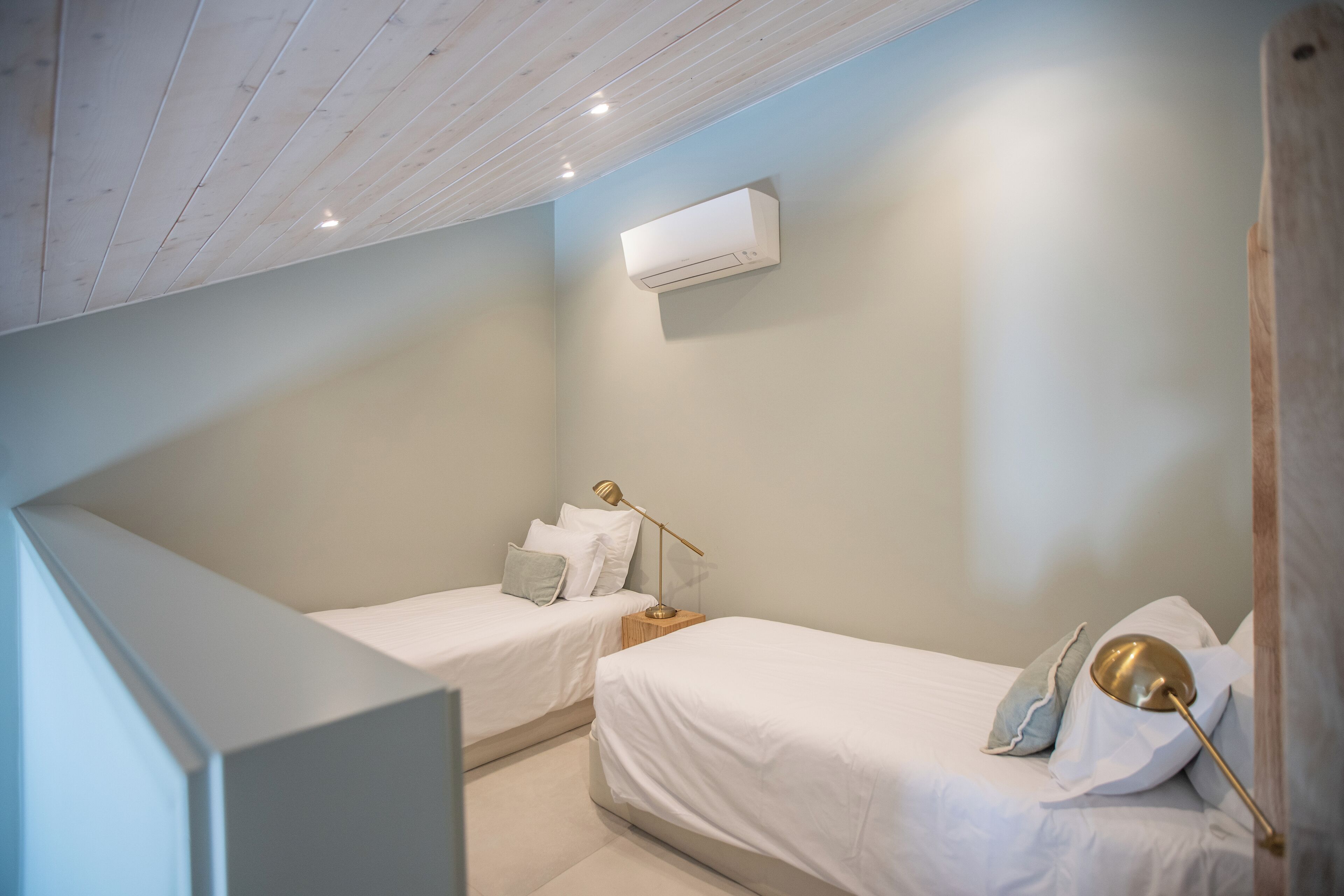 A bedroom with two single beds, a ceiling fan, and an air conditioning unit.