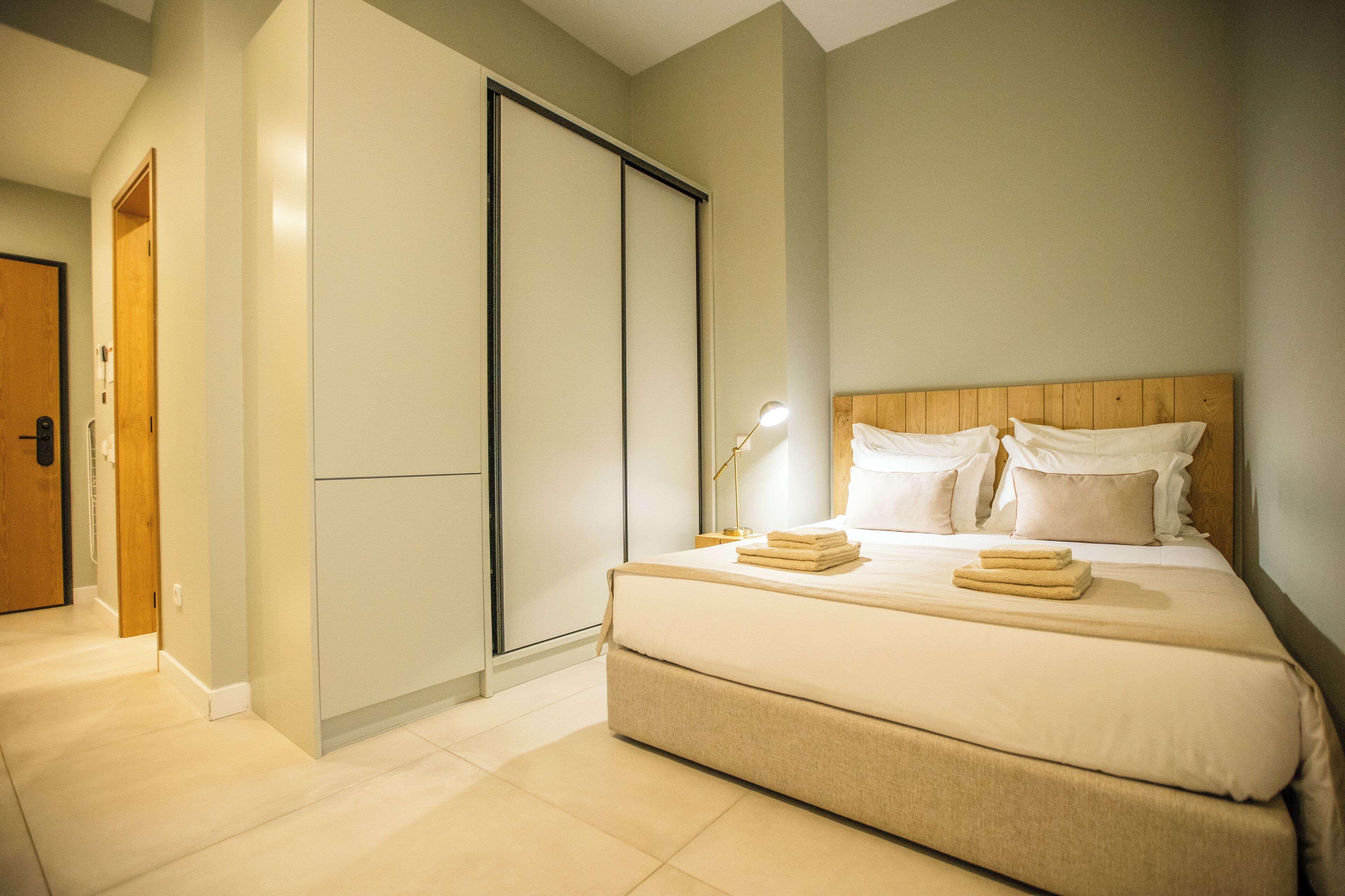 Een slaapkamer met een bed, nachtkastje, lamp en een kledingkast.