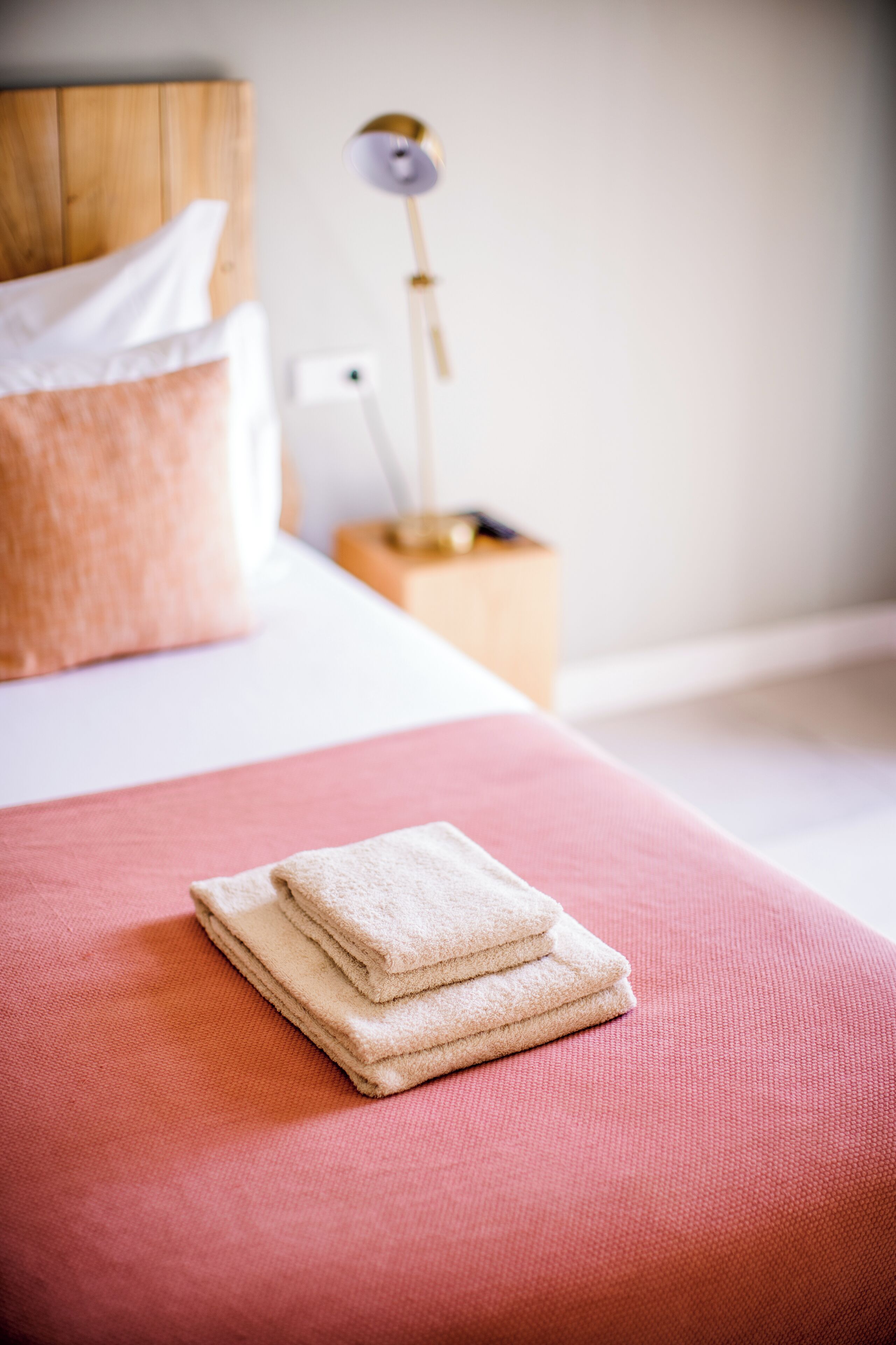 A neatly made bed with a pink bedspread and a stack of white towels.