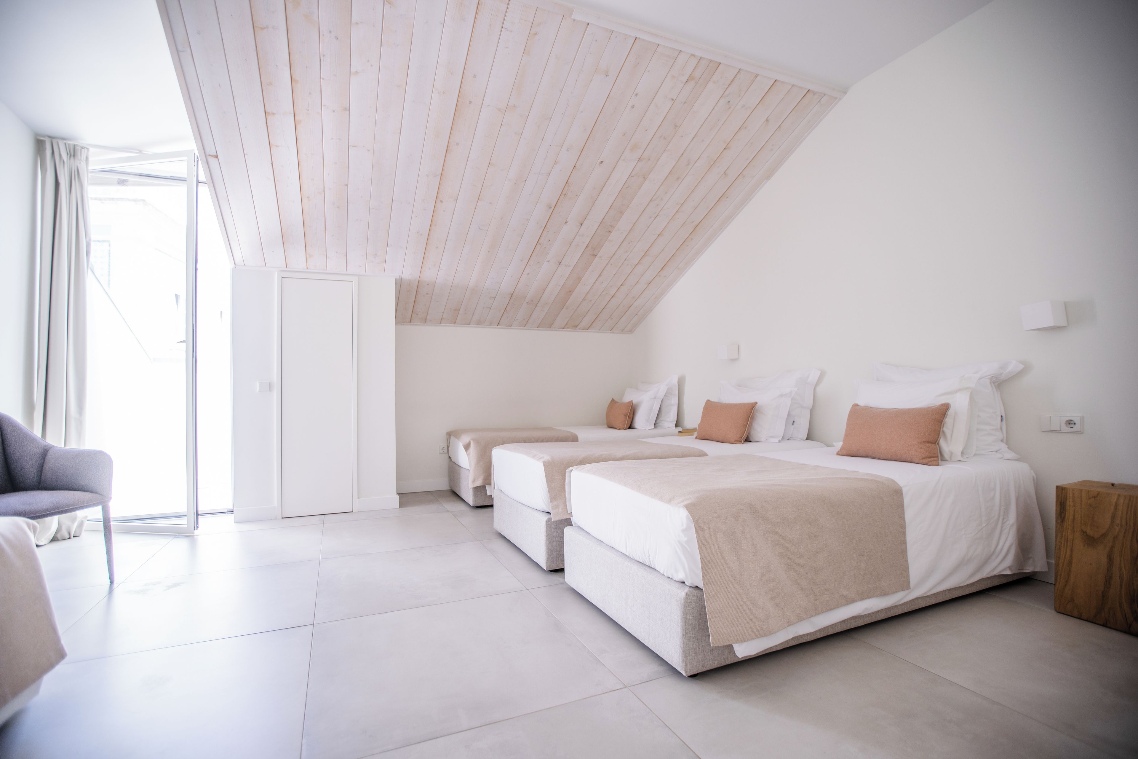 A modern bedroom with two beds, a large window, and a sloped ceiling.
