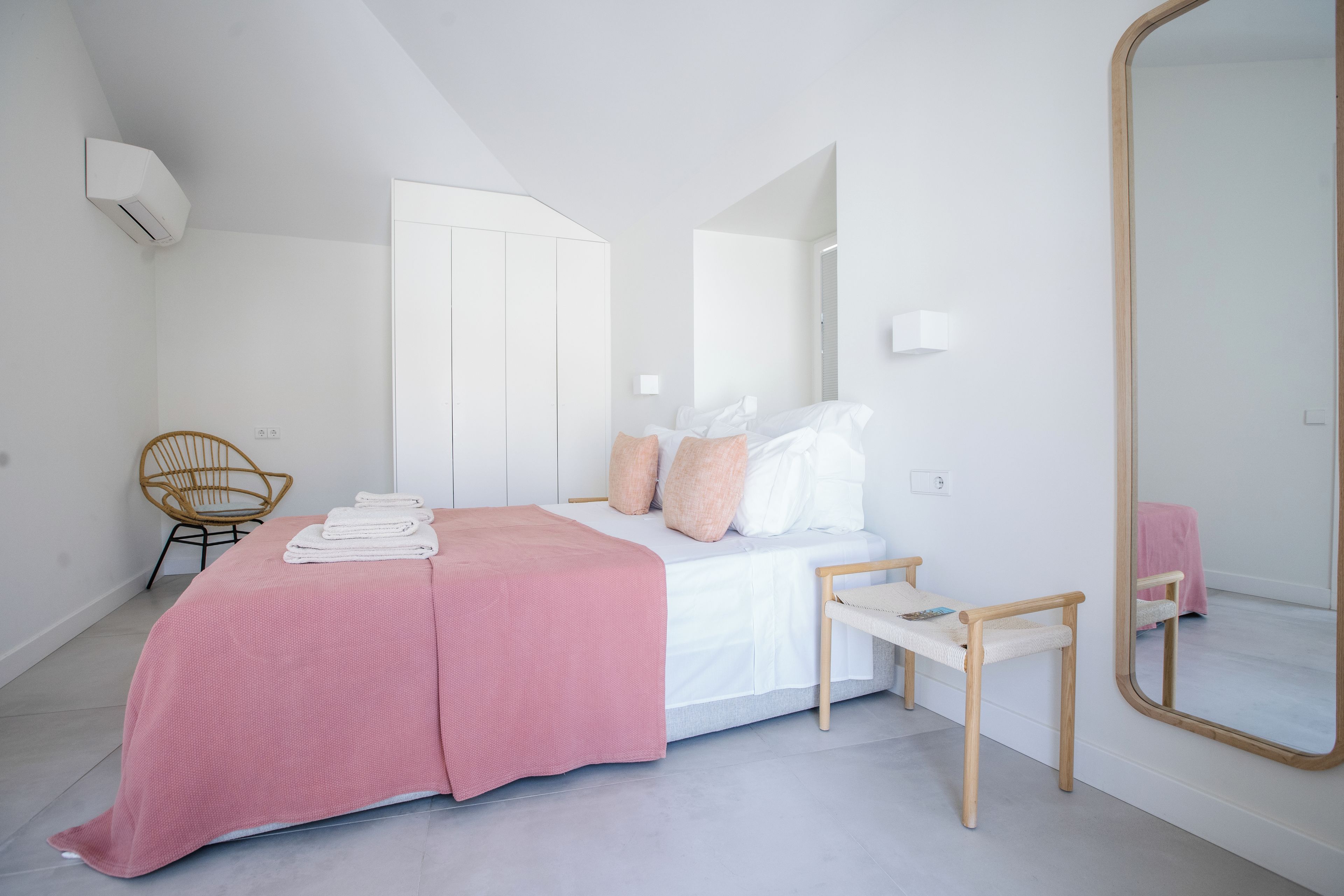 Un dormitorio con cama, una silla, una mesita y un espejo.