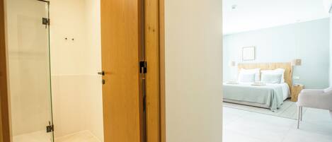 A hotel room with a wooden door, a glass shower enclosure, a bed with white bedding, and a nightstand.