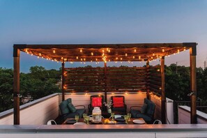 An outdoor patio with a wooden pergola, string lights, and a table set for dining. - Eclectic Austin Oasis| Rooftop Decks, Downtown Views (Austin)