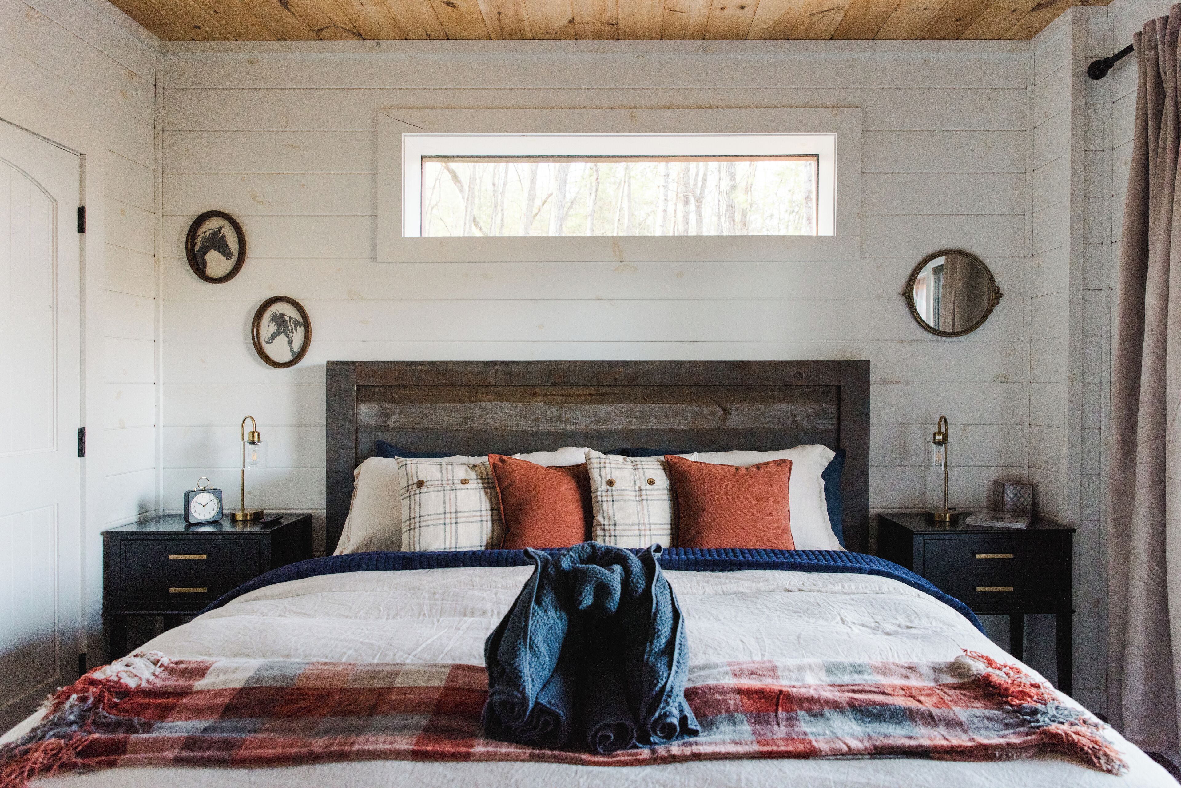A bedroom with a wooden headboard, a large window, and a plaid blanket on the bed.