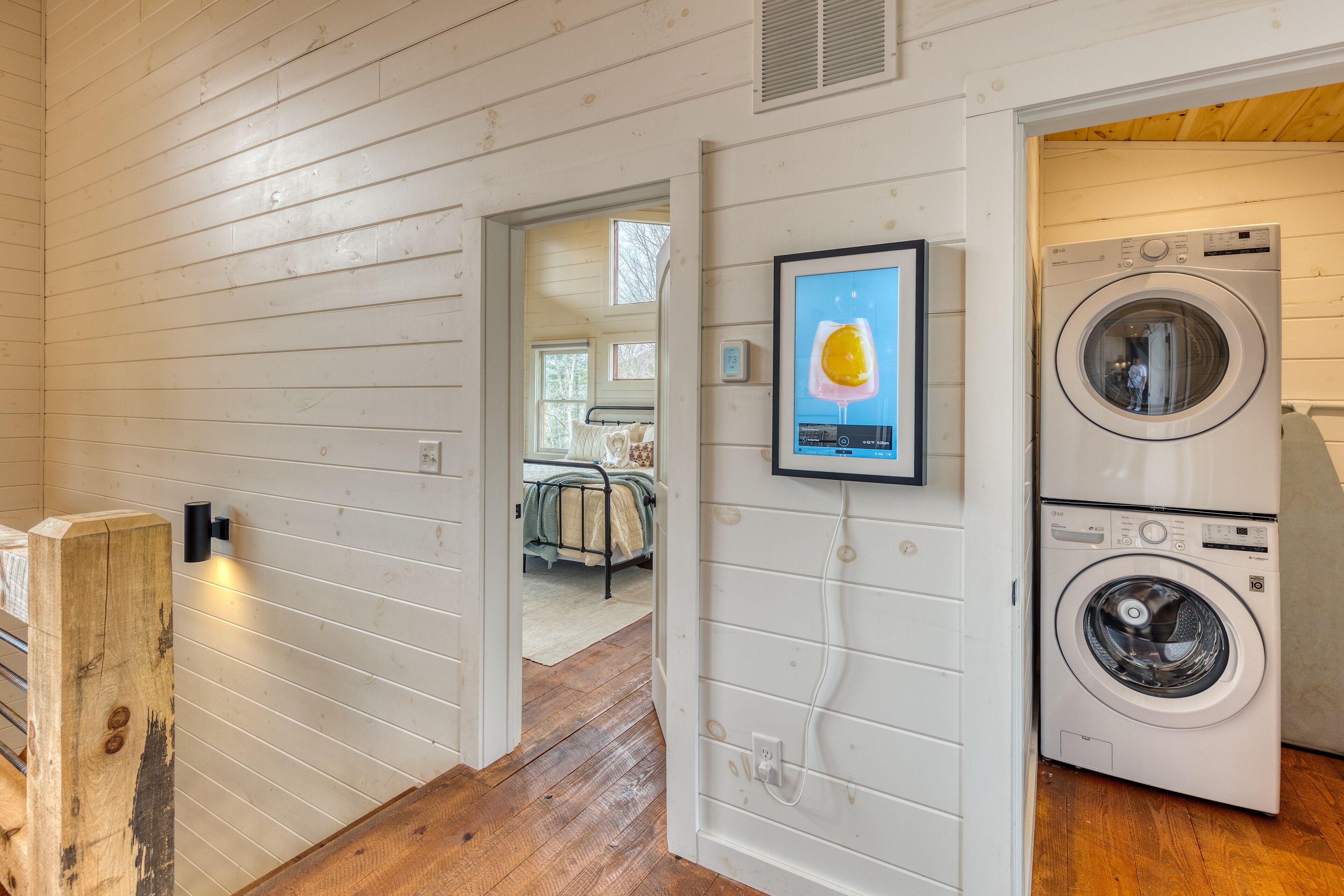 A laundry area with a washing machine and dryer, a wooden floor, and a framed picture on the wall.