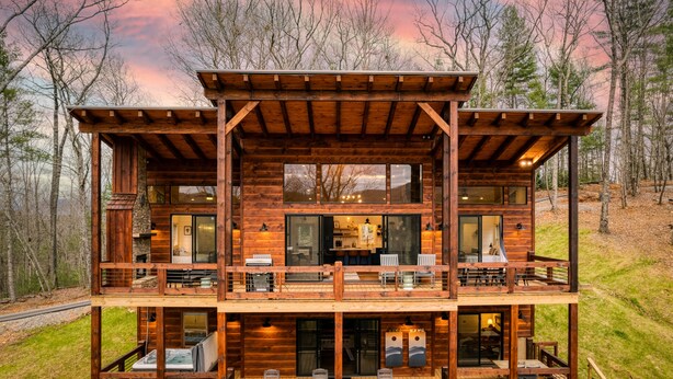 Een houten blokhut met twee verdiepingen, een balkon en een hottub op de begane grond.