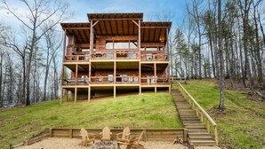 Een houten vakantiehuis met meerdere verdiepingen, een terras, een vuurkuil en zitplaatsen buiten.