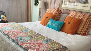 Een net opgemaakt bed met een kleurrijke quilt, gestreepte kussens en een ingelijst beeld aan de muur.