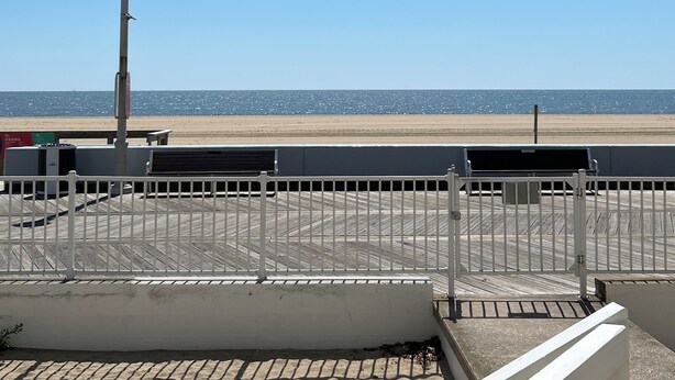 Uitzicht op een strand vanaf een beschutte plek, met een metalen hekwerk, een lantaarnpaal en een bank.