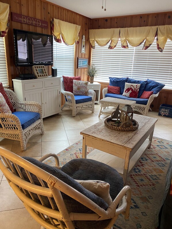 A cozy living room with wicker furniture, a television, and a wooden wall. - Oceanfront - Cozy Condo on 25th street & boardwalk (Ocean City)