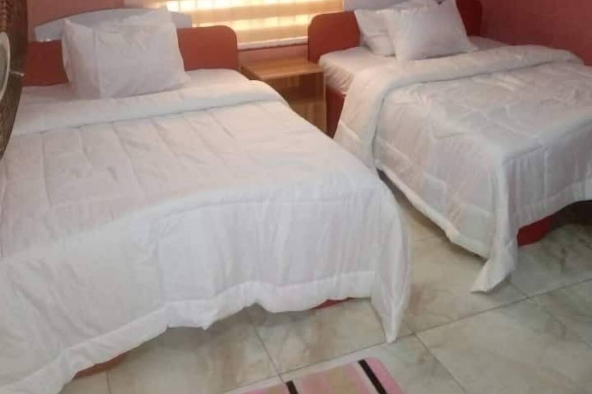 Una habitación con dos camas individuales, una mesita y una ventana con persianas.