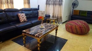A living room with a black leather sofa, a marble coffee table, a striped ottoman, and a small side table with a vase. - Biddex Lodge - by Cenlotts (Benin City)