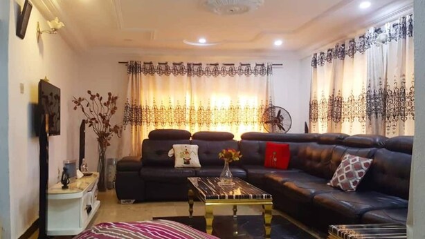 A living room with a dark leather sofa, a striped ottoman, a coffee table, and a side table with a vase. - Biddex Lodge - by Cenlotts (Benin City)