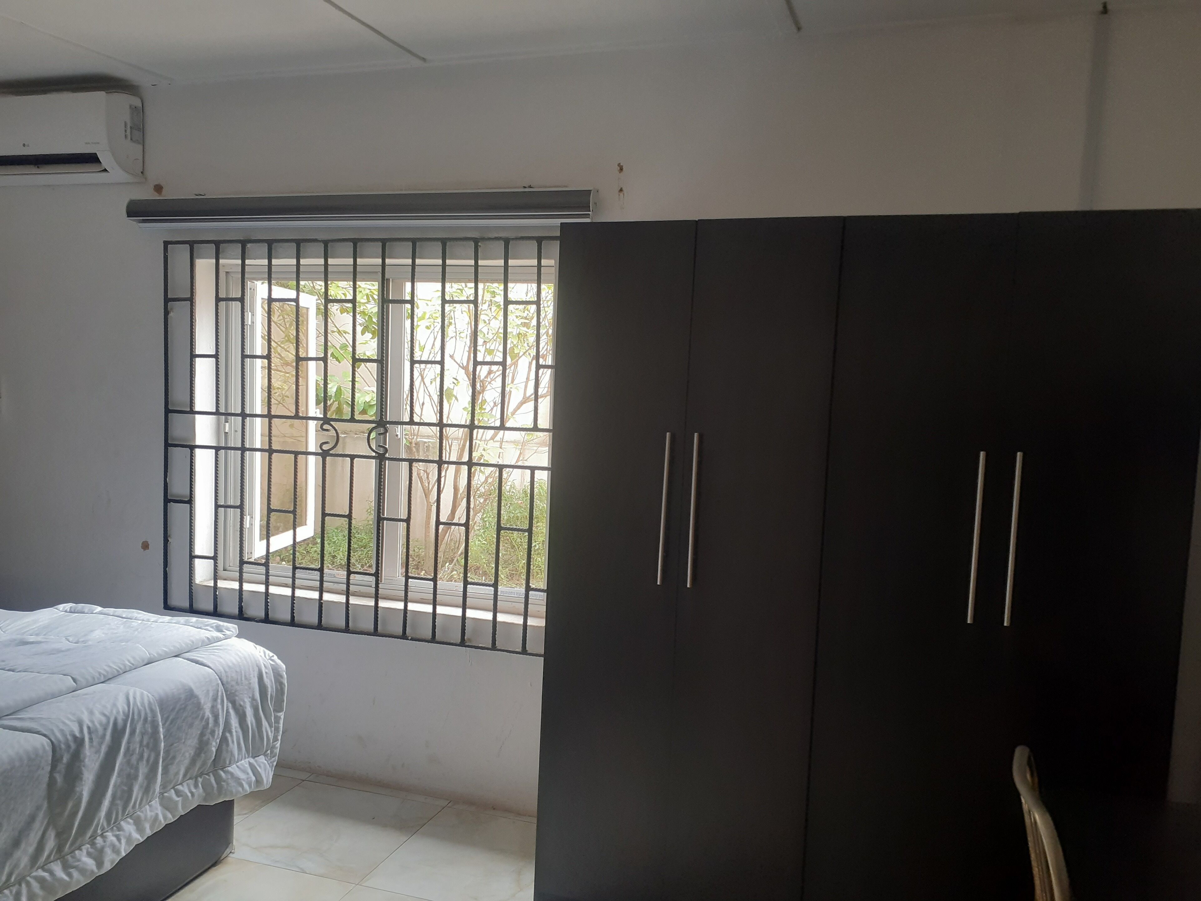 A bedroom with a bed, a wardrobe, and a window with a metal grill.
