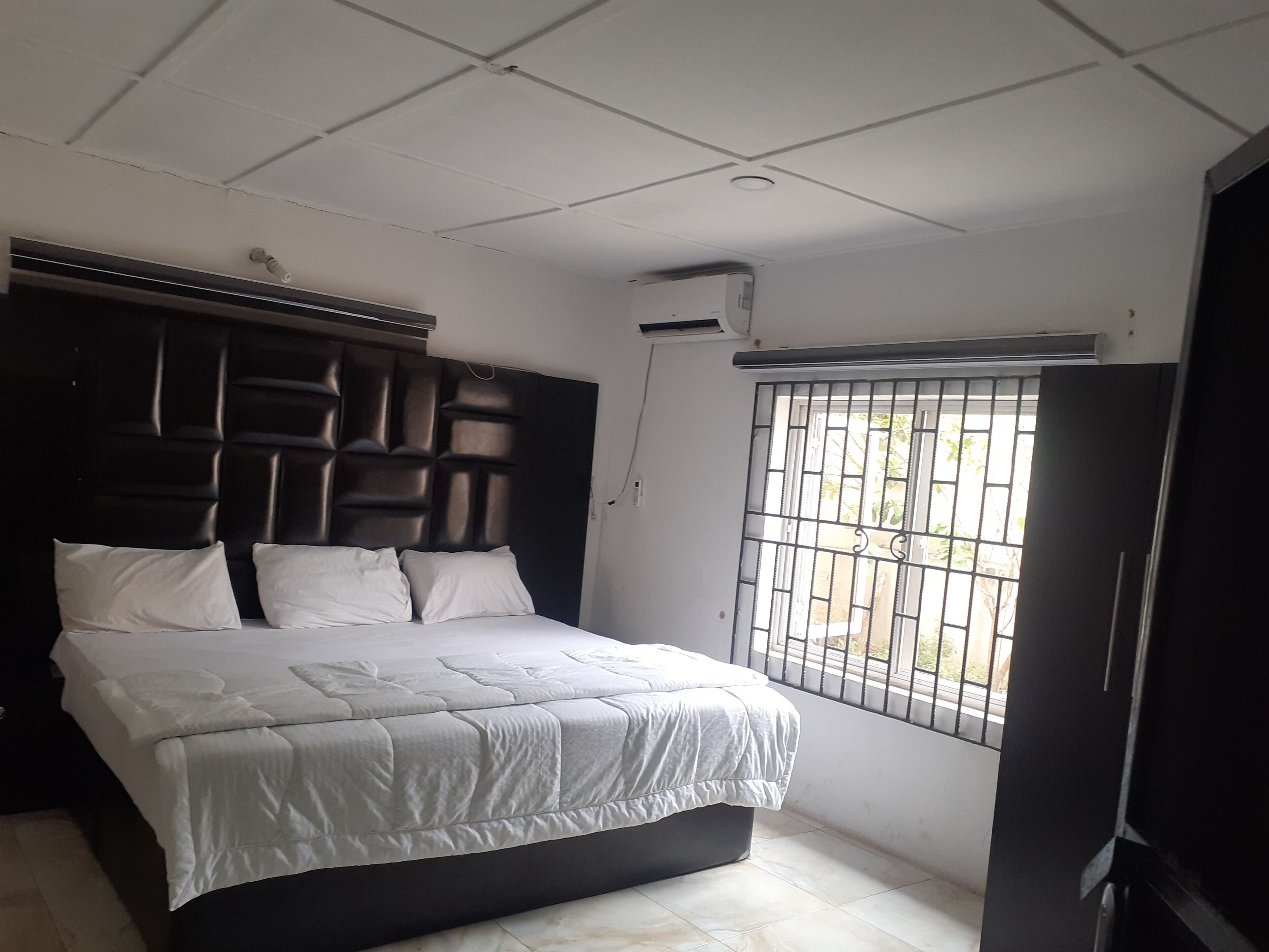 A bedroom with a bed, a headboard, a window with bars, and an air conditioning unit.