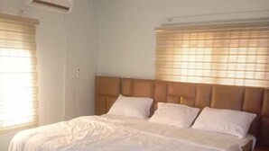 A bedroom with a large bed, a wooden headboard, and a window with blinds. - Biddex Lodge - by Cenlotts (Benin City)