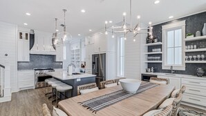 Une cuisine moderne avec des meubles blancs, un îlot central et un coin repas comprenant une table en bois et des tabourets de bar.