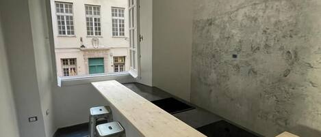 A narrow kitchen with a long counter, three stools, and a window overlooking a building.