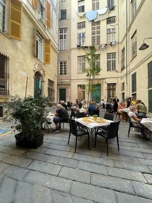 A courtyard with outdoor seating, surrounded by buildings with balconies and shutters. - Happy Family Apartments Sauli (Genoa)