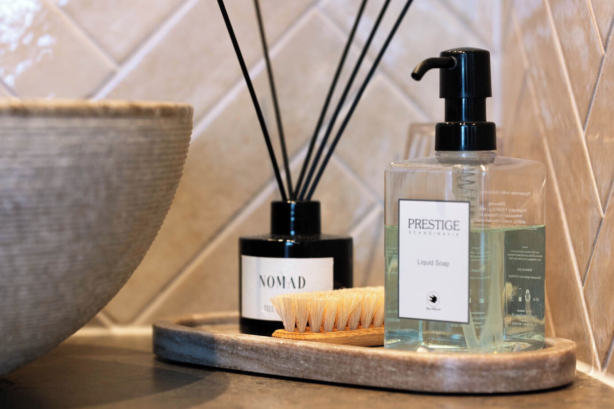 A bathroom with a soap dispenser, a bottle of liquid soap, and a brush on a tray.